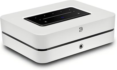 Integrovaný stereo hi-fi zesilovač BlueSound Powernode 2025 (N331) v bílé barvě, bílý matný plastový obdélníkový kryt s centrální černou drážkou, černý lesklý dotykový panel zapuštěný na horní straně, stylizované logo a 3,5mm jack konektor na přední straně, pohled zepředu v tříčtvrtečním úhlu