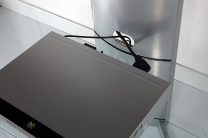 Norstone Design Mask AV grå audio-/videomøbel, set ovenfra i et dykkende perspektiv, med en dekoder placeret oven på og sorte kabler