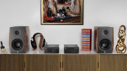 Sistema hi-fi Gold Note con diffusori da scaffale in noce, amplificatori compatti neri e cuffie su mobile di design sotto quadro