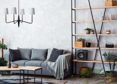Moderne stue med grå sofa, puder, træhylder, planter, sorte hængelamper og lyse gråbetonvægge
