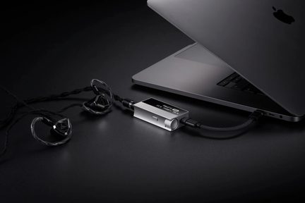 Портативний сріблястий DAC з коліщатком, під’єднаний до MacBook і чорних внутрішньоканальних навушників