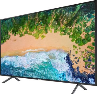 Samsung UE49NU7105-fladskærm, der viser en sandstrand og turkisblå bølger med en grøn tropisk skov i baggrunden