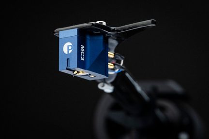 Cellula fonografica blu con connettori dorati, fissata a un braccio di lettura nero inclinato, sfondo nero uniforme