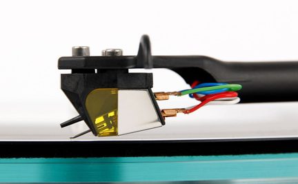 Side view of black phono cartridge, copper connectors, red, green, blue, white wires, diamond tip, vinyl surface