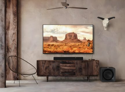 Fernseher, der eine felsige Wüstenlandschaft zeigt, auf einem Möbel aus rohem Holz in einem Raum mit Betonwänden und Dekorationen