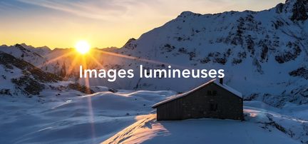 Chalet en bois enneigé au soleil couchant dans les montagnes enneigées avec un ciel orangé et bleu au crépuscule