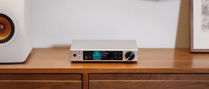 Silberner Audioverstärker aus gebürstetem Aluminium, Frontansicht, schlankes rechteckiges Gehäuse mit zentralem Farbdisplay, zwei runde Kopfhöreranschlüsse links und großer schwarzer Lautstärkeregler mit Metallring rechts