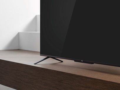 TCL 65C721 sort fladskærms-TV i sort, stående på et træmøbel, set fra en trekvartvinkel