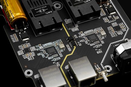 Sort elektronisk printkort med to RJ45-porte, gylden kondensator og SMD-komponenter i nærbillede