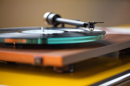 Un giradischi in legno con un vinile nero, un braccio di lettura metallico e una puntina visibile in primo piano