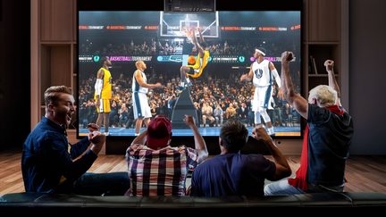 Televisore a grande schermo in un soggiorno, partita di basket sullo schermo e quattro tifosi di spalle in festa