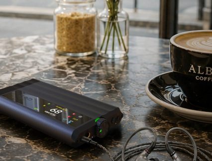 Lettore audio digitale nero con schermo touch, rotella del volume e auricolari su un tavolino da caffè