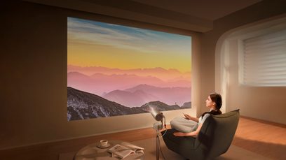 Videoproiettore XGIMI MoGo 3 Pro, immagine proiettata paesaggio montuoso, donna seduta poltrona, tavolino tazza libro