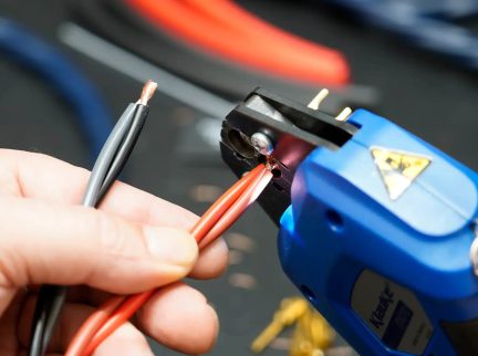 Automatische draadstripper van Klein Tools in blauw in close-up op rode en zwarte elektrische kabels