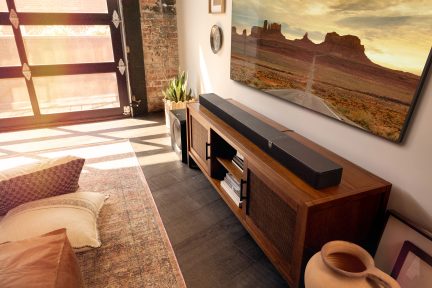 Indvendig udsigt af en stue med et træmøbel, en soundbar, et vægmaleri, puder, en plante og en glasdør