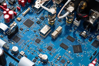 Sidabrinis garso keitiklis DAC RD160, artimas elektroninių komponentų vaizdas ant mėlynos pagrindinės plokštės, raudoni kondensatoriai, metaliniai jungtys.