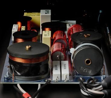 Passive Frequenzweiche für Lautsprecher mit orangefarbenen und schwarzen Spulen, roten Kondensatoren und weißen Widerständen, in Nahaufnahme