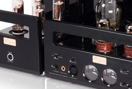 Primo piano in vista tre quarti anteriore di un amplificatore audio a valvole in metallo spazzolato nero, dotato di valvole a vuoto in vetro incandescente, tre VU-metri circolari, un pulsante di accensione luminoso e diverse prese per cuffie sul pannello frontale