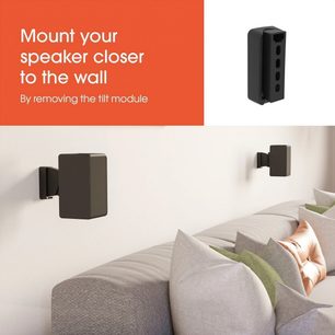 Suporte de parede para coluna Vogel's SWM 3021 preto, com colunas pretas fixadas por cima de um sofá cinzento