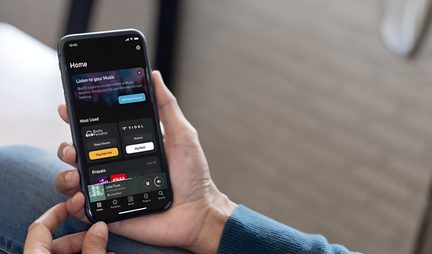 Smartphone preto com ecrã de vidro, interface musical escura e barra de reprodução, segurado na mão, vista em três quartos