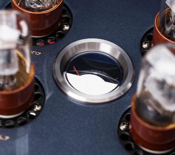 Nærbillede set ovenfra af en Cayin CS-88A KT88 integreret stereo rørforstærker, blåmetallic chassis med cirkulært vindue indrammet af børstet stål, der viser en rød nål og glasrør monteret på kobberbrune sokler