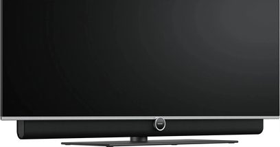 Schwarze Loewe Antares Soundbar unter einem Fernseher mit silberner zentraler Kreissteuerung