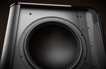 Sort subwoofer med stor cirkulær højttaler og tekstureret gitter, set tæt på