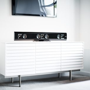 Mobile TV bianco con 3 cassetti, sovrastato da una soundbar nera Klipsch Gallery G-42 sotto uno schermo TV a parete