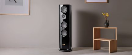 Altavoz de columna hi-fi Canton negro lacado con cuatro altavoces en un salón moderno con estantería de madera