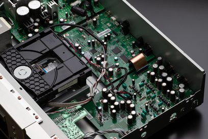 Placa de circuito impresso verde com componentes eletrônicos, condensadores e cabos em uma caixa metálica, vista superior