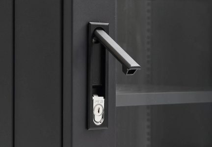Rechthoekige zwarte handgreep met geïntegreerd zilverkleurig slot op een zwarte deur, glazen plank zichtbaar op de achtergrond