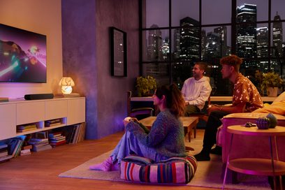 Moderne stue med to menn som sitter på en sofa, en kvinne som sitter på en puff, foran et vindu med utsikt over opplyste skyskrapere om natten