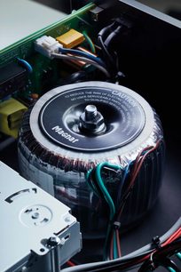 Set ovenfra af en Magnat toroidal transformer med farvede kabler tilsluttet og teksten "To reduce the risk of electric shock"