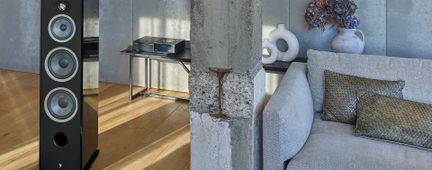 Svart, lakkert gulvstående høyttaler sett forfra, med tre grå elementer, diskant og bassrefleksport, ved siden av en betongsøyle