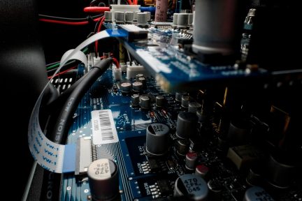 Nærbillede af et blåt elektronikkort med kondensatorer, kabler og internt forbindelsesbåndkabel