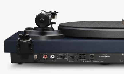 Tumši zils vinila plašu atskaņotājs, skats no aizmugures, ar melnu disku, RCA izejām un Bluetooth vadības pogām
