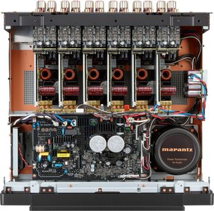 Потужний багатоканальний підсилювач Marantz AMP 20, вид зсередини спереду, чорний металевий корпус з мідними елементами та кількома вертикальними модулями з чорними друкованими платами, мідними котушками, циліндричними сірими конденсаторами та круглим тороїдальним трансформатором чорного кольору з логотипом