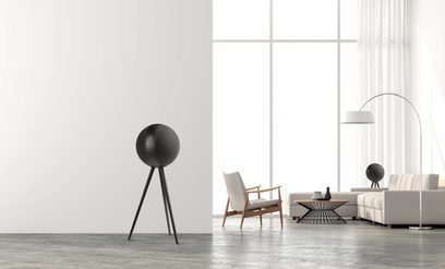 Sort, sfærisk højttaler på sort trebenet stativ, moderne hvide lænestol og sofa i et minimalistisk, hvidt interiør