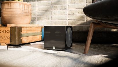 Subwoofer SVS 3000 Micro negru lucios, vedere frontală, așezat pe un covor, înconjurat de obiecte din lemn