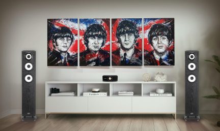 Four colorful paintings aligned above a white piece of furniture with two vertical black speakers on each side