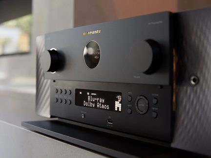 Black metal AV amplifier, two large knobs, circular and rectangular displays, front USB port, angled view
