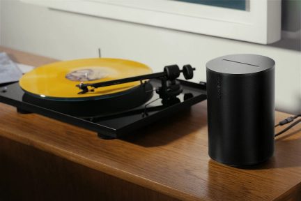 Plato de vinilo negro con disco amarillo y altavoz negro sobre mueble de madera
