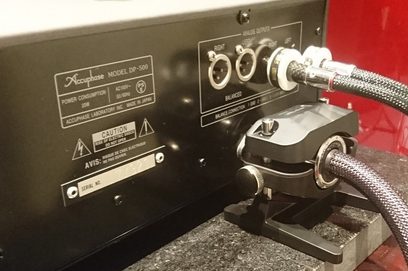 Furutech NCF Booster DP-500 cable accessory, rear view showing connectors and settings, placed on a red granular surface