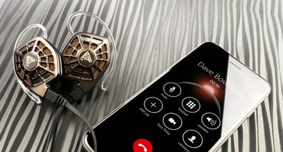 Audeze iSINE 20 hovedtelefoner og smartphone, der viser Audeze-applikationsgrænsefladen, placeret på en stribet grå og hvid baggrund