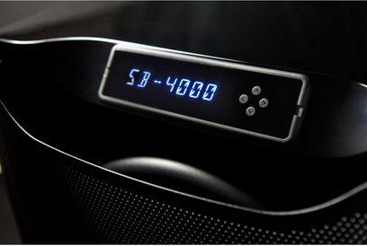 Blåt digitalt display der viser "SB-4000" på en sort lakeret SVS subwoofer, nærbillede