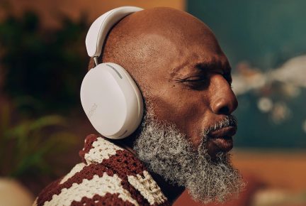 Baltā Sonos audio aurikuli, kas nospiesti uz profila persona ar zilām brīnumiem un brīna un baltā strīkotāja puloveri