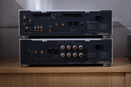 Zadní pohled na dva černé kovové hi‑fi audio přístroje naskládané na sobě, porty RCA, XLR a HDMI, reproduktorové svorky, síťová zásuvka