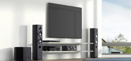 Sort vægmonteret tv, 2 sorte gulvhøjttalere, 1 subwoofer, 1 afspiller, 1 forstærker, 1 hvidt møbel