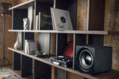 Velodyne Deep Blue 10 sort subwoofer i sort på en træhylde, med bøger og vinylplader i baggrunden