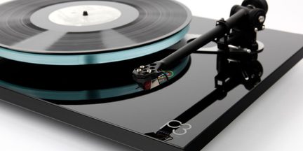 Vista em ângulo de um toca-discos preto com braço de leitura preto e disco de vinil sobre prato transparente